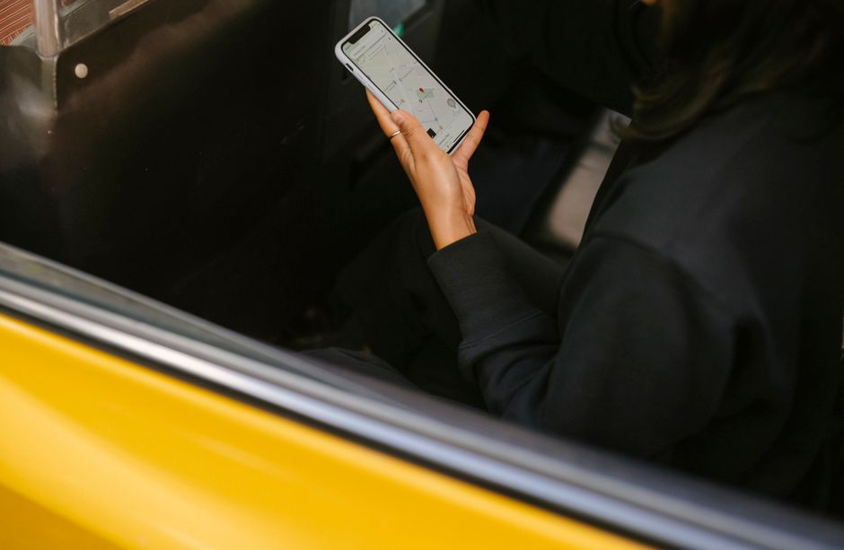 From above side view of crop anonymous woman watching cellphone with map application on screen while travelling in yellow transport
